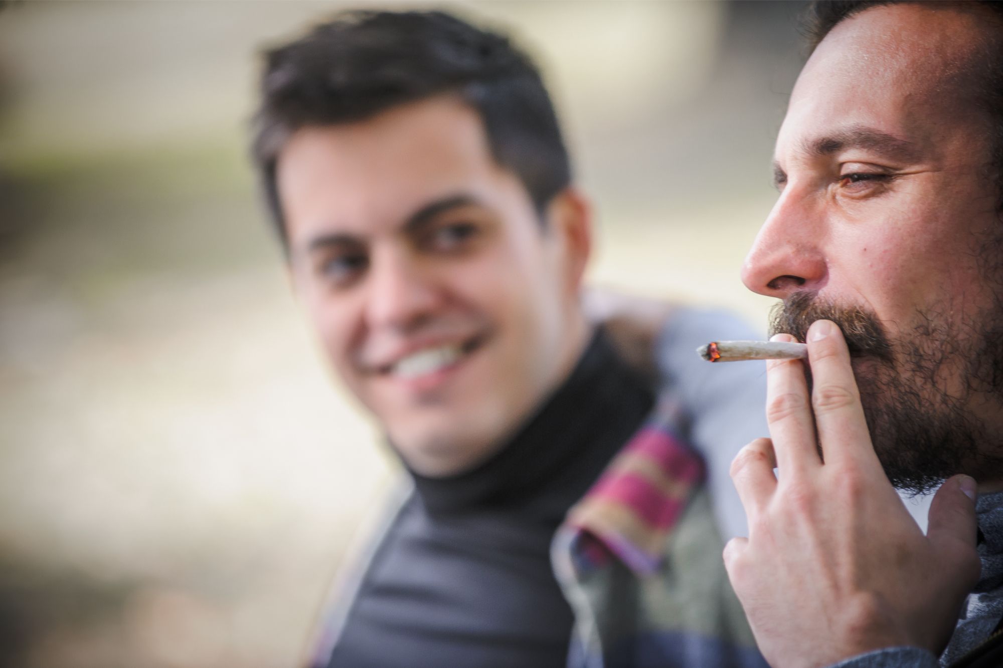 A man smoking weed smoking weed in denver while his friend looks at him and smiles, enjoying a relaxed moment together.