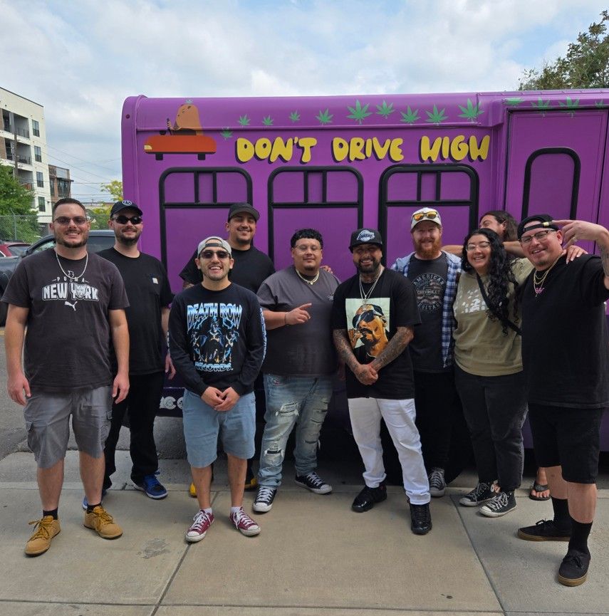 A group of people smiling and posing in front of a purple cannabis-themed tour bus with the message “Don’t Drive High” painted on the side. The group stands on a sidewalk in a casual outdoor setting, promoting safe and responsible cannabis consumption The Ultimate 420-Friendly Vacation Guide